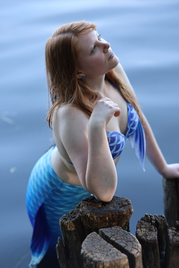 Kimi-chan als anmutig stehende Meerjungfrau gen Himmel schauend vor ruhigem seichtem Wasser.