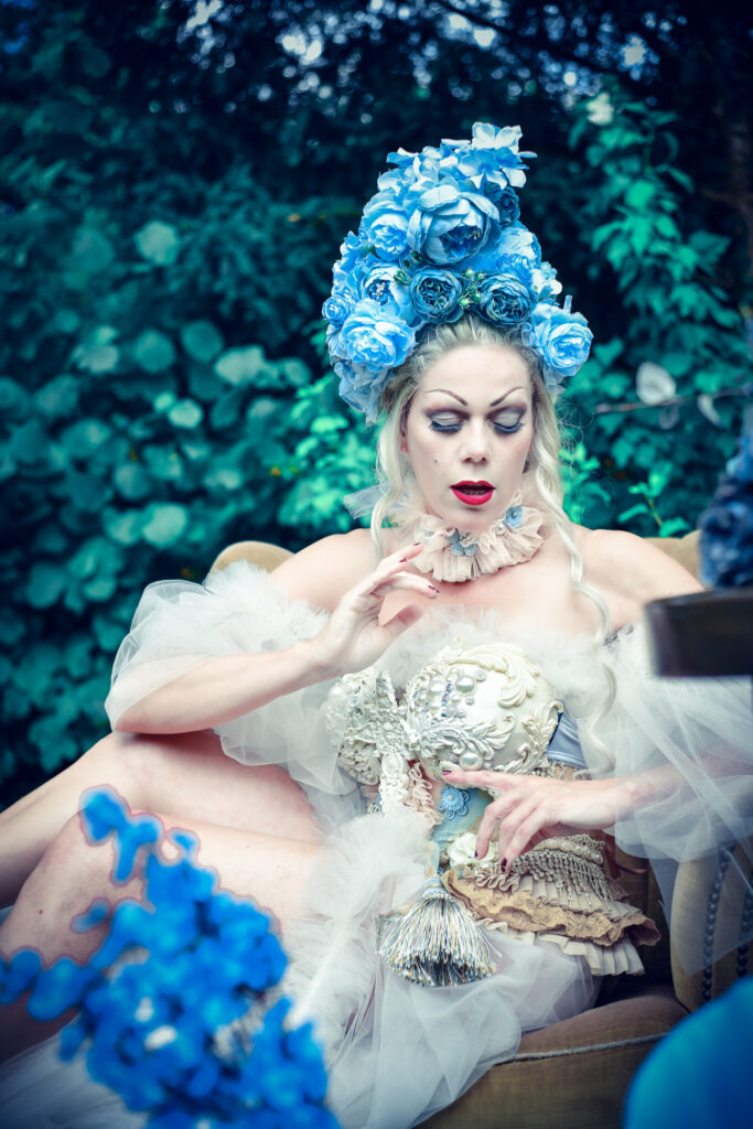 Das Fantasy-Portrait zeigt eine Frau mit einer Korsage im Barock-Stil und einem extravagantem blauen Blumen-Kopfschmuck.