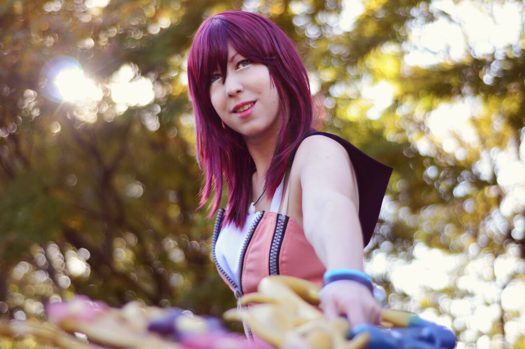 Cosplayerin Traumblume im Cosplay aus dem Spiel Kingdom Hearts. Sie hält ihren Schlüssel und ist von einem Lichterbouquet und vielen Bäumen umgeben.