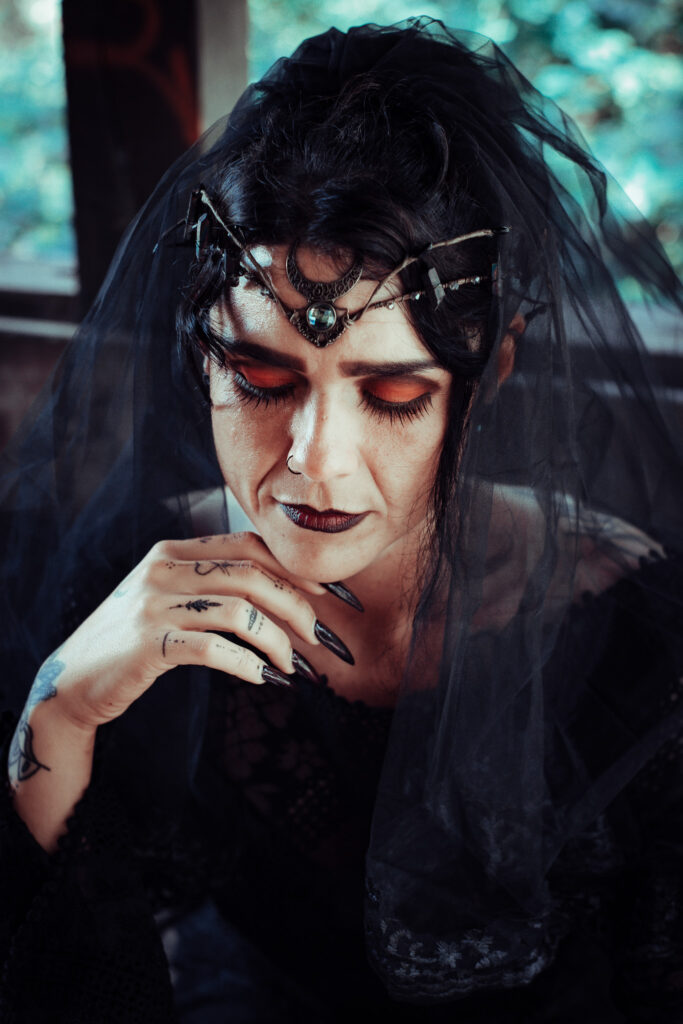 Fantasy-Porträt einer Hexe mit schwarzem Schleier, Kopfschmuck und langen schwarzen Nägeln beim Ritual.