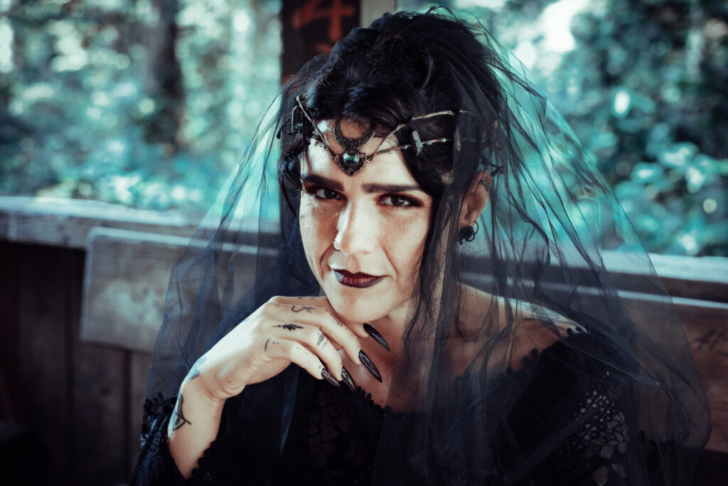 Fantasy-Hexe mit schwarzem Schleier und dunklem Makeup, die intensiv in die Kamera blickt.