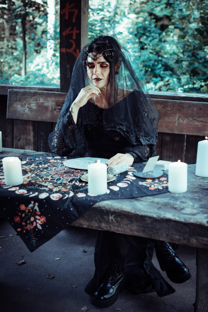 Hexe mit schwarzem Schleier sitzt an einem Ritualtisch mit Kerzen bei einem magischen Fantasy-Fotoshooting.