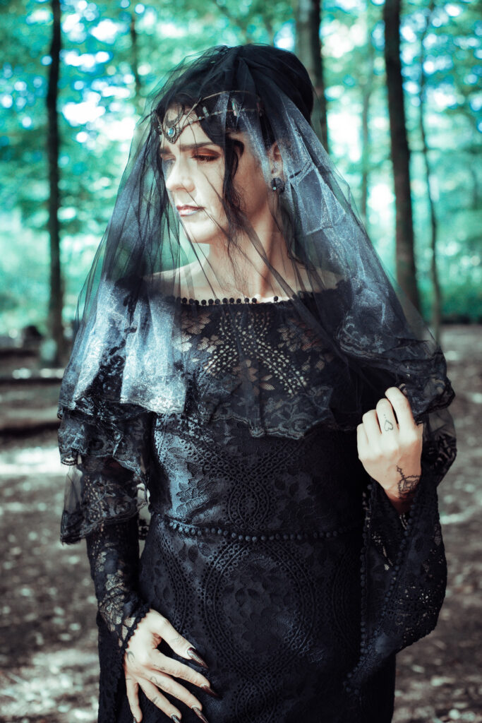 Nahaufnahme einer Hexe mit dunklem Schleier, starkem Makeup und mystischer Ausstrahlung.